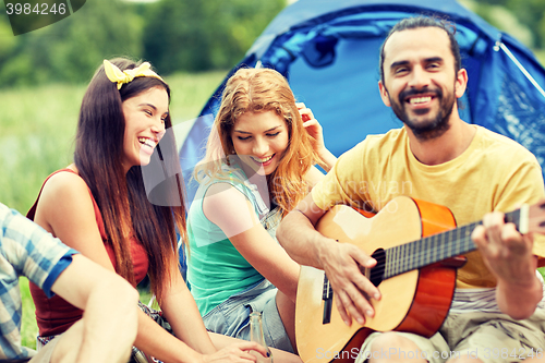 Image of happy friends with drinks and guitar at camping