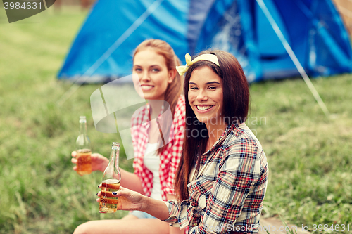 Image of happy young women with tent and drinks at campsite