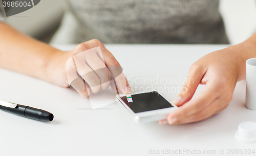 Image of close up of woman with smartphone doing blood test