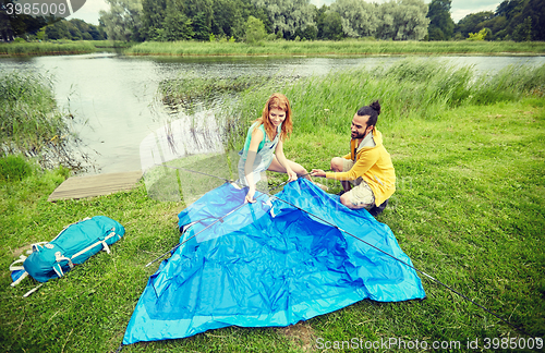 Image of happy couple setting up tent outdoors