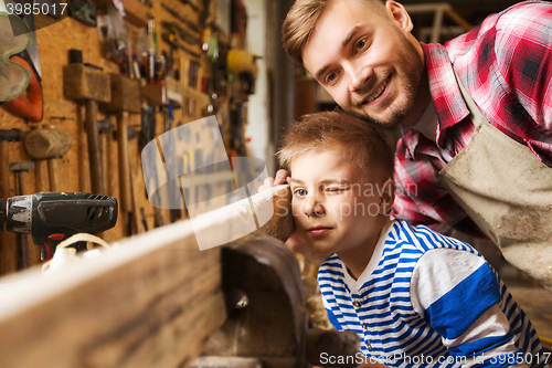 Image of father and little son with wood plank at workshop