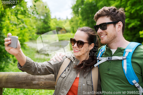 Image of couple with backpacks taking selfie by smartphone