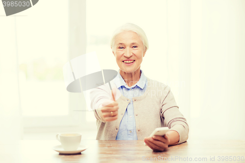 Image of senior woman with smartphone showing thumbs up