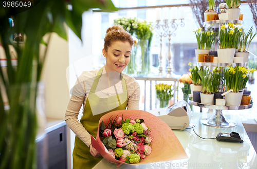 Image of smiling florist woman packing bunch at flower shop