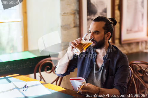 Image of man with notebook drinking beer at bar or pub
