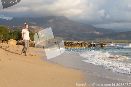 Image of Woman walking on sand beach at golden hour