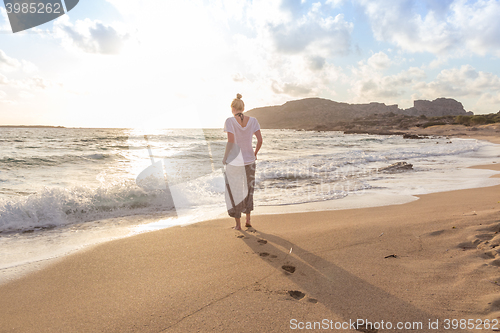 Image of Woman walking on sand beach at golden hour