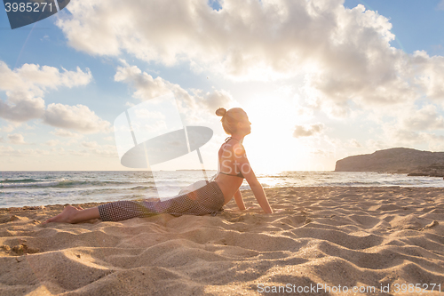 Image of Woman practicing yoga on sea beach at sunset.