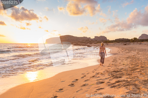 Image of Woman walking on sand beach at golden hour