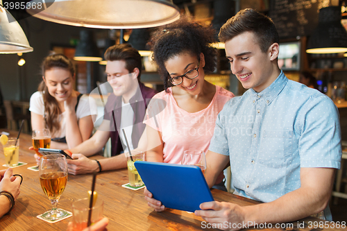 Image of happy friends with tablet pc and drinks at bar