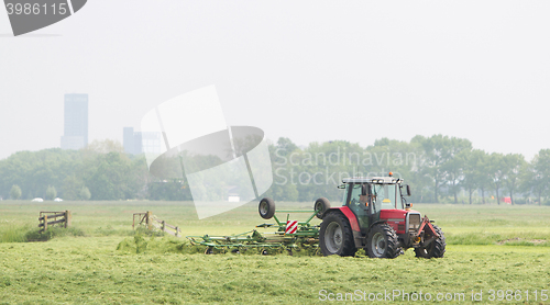 Image of Farmer uses tractor to spread hay on the field