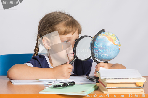 Image of Six-year girl sitting at the table and looks at the globe through a magnifying glass