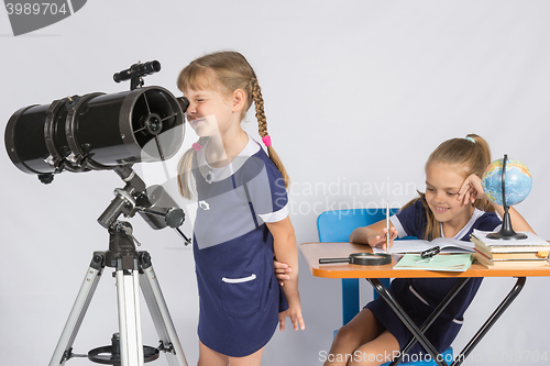 Image of Girl astronomer looks through the eyepiece of the telescope, and the other girl sitting happily at the table