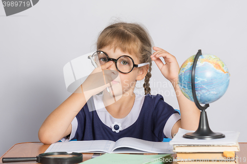 Image of Schoolgirl corrects glasses while sitting at a desk in the classroom Geography