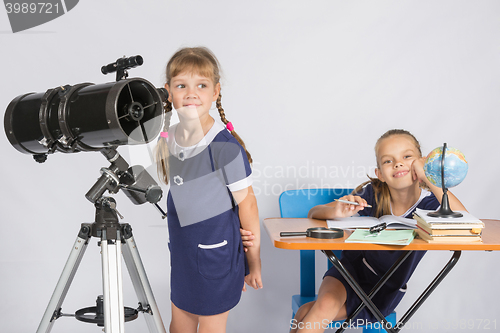 Image of Girl astronomer looks at the sky, the other girl sitting happily at the table