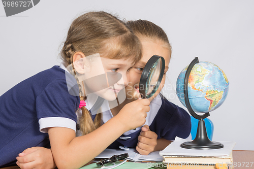 Image of Two girls girlfriends looking at globe through a magnifying glass