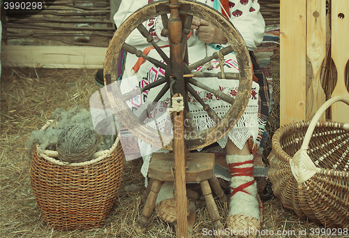 Image of An elderly woman spinning thread on a spinning wheel.