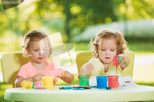 Image of Two-year old girls painting with poster paintings together against green lawn