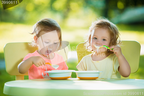 Image of Two little girls sitting at a table and eating together against green lawn