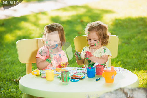 Image of Two-year old girls painting with poster paintings together against green lawn