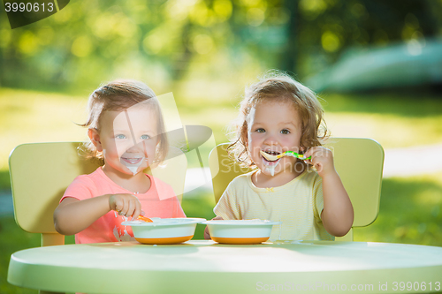 Image of Two little girls sitting at a table and eating together against green lawn