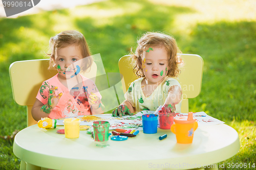 Image of Two-year old girls painting with poster paintings together against green lawn