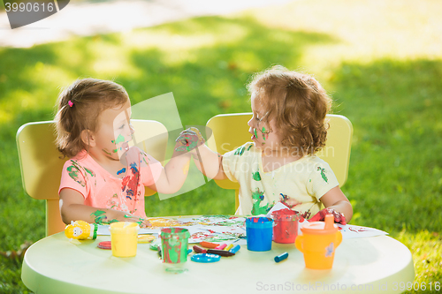 Image of Two-year old girls painting with poster paintings together against green lawn