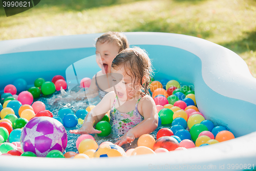 Image of The two little baby girls playing with toys in inflatable pool in the summer sunny day