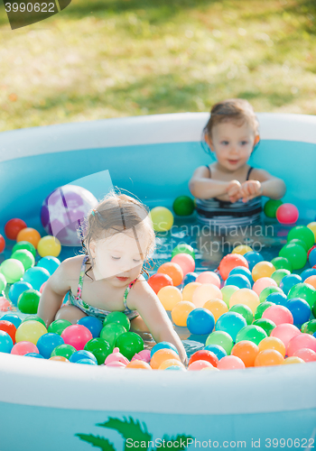 Image of The two little baby girls playing with toys in inflatable pool in the summer sunny day