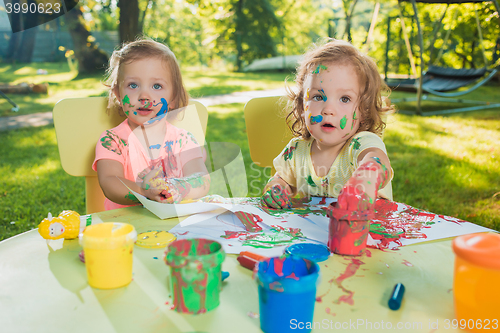 Image of Two-year old girls painting with poster paintings together against green lawn