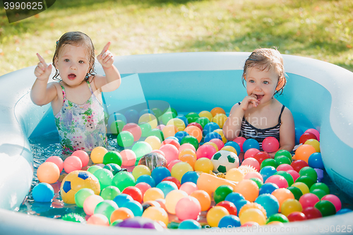 Image of The two little baby girls playing with toys in inflatable pool in the summer sunny day