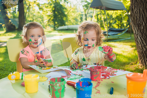 Image of Two-year old girls painting with poster paintings together against green lawn