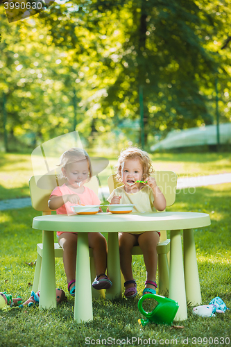 Image of Two little girls sitting at a table and eating together against green lawn