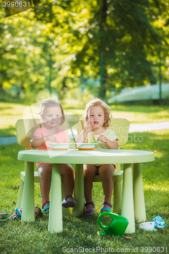 Image of Two little girls sitting at a table and eating together against green lawn