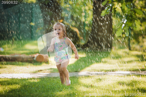 Image of The little baby girl playing with garden sprinkler.