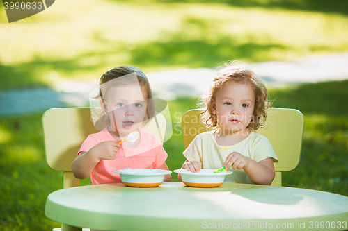 Image of Two little girls sitting at a table and eating together against green lawn