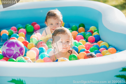 Image of The two little baby girls playing with toys in inflatable pool in the summer sunny day