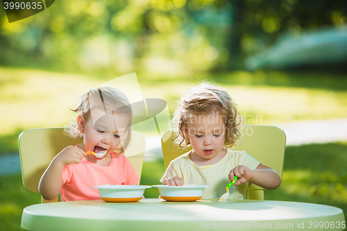 Image of Two little girls sitting at a table and eating together against green lawn