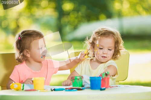 Image of Two-year old girls painting with poster paintings together against green lawn