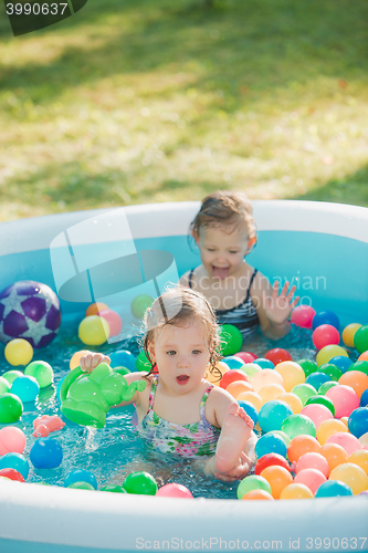 Image of The two little baby girls playing with toys in inflatable pool in the summer sunny day