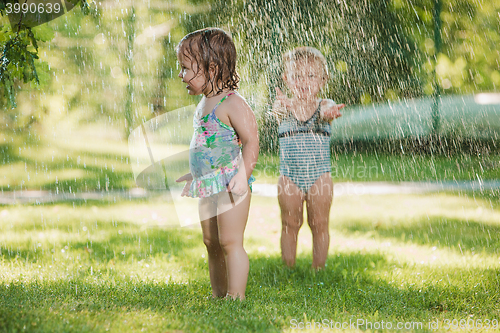 Image of The two little baby girls playing with garden sprinkler.