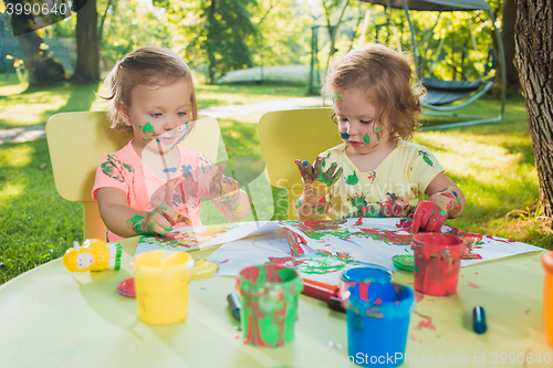 Image of Two-year old girls painting with poster paintings together against green lawn