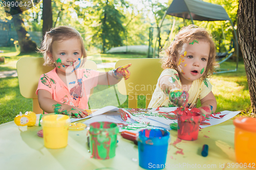 Image of Two-year old girls painting with poster paintings together against green lawn