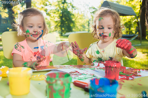 Image of Two-year old girls painting with poster paintings together against green lawn