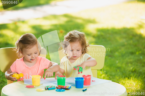 Image of Two-year old girls painting with poster paintings together against green lawn