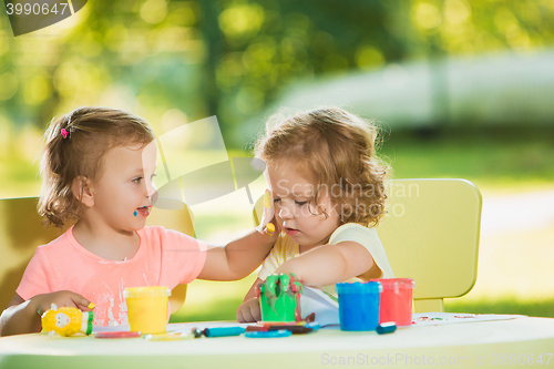 Image of Two-year old girls painting with poster paintings together against green lawn