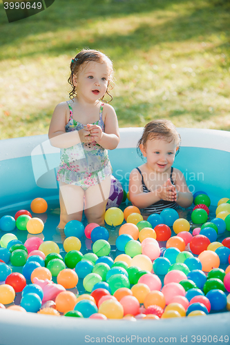 Image of The two little baby girls playing with toys in inflatable pool in the summer sunny day