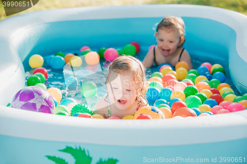 Image of The two little baby girls playing with toys in inflatable pool in the summer sunny day