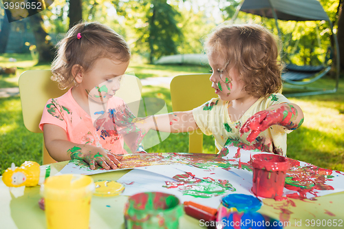 Image of Two-year old girls painting with poster paintings together against green lawn