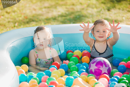 Image of The two little baby girls playing with toys in inflatable pool in the summer sunny day